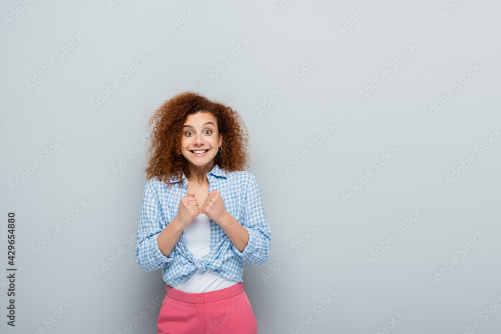 Fototapeta premium amazed woman showing luck gesture while looking at camera on grey background