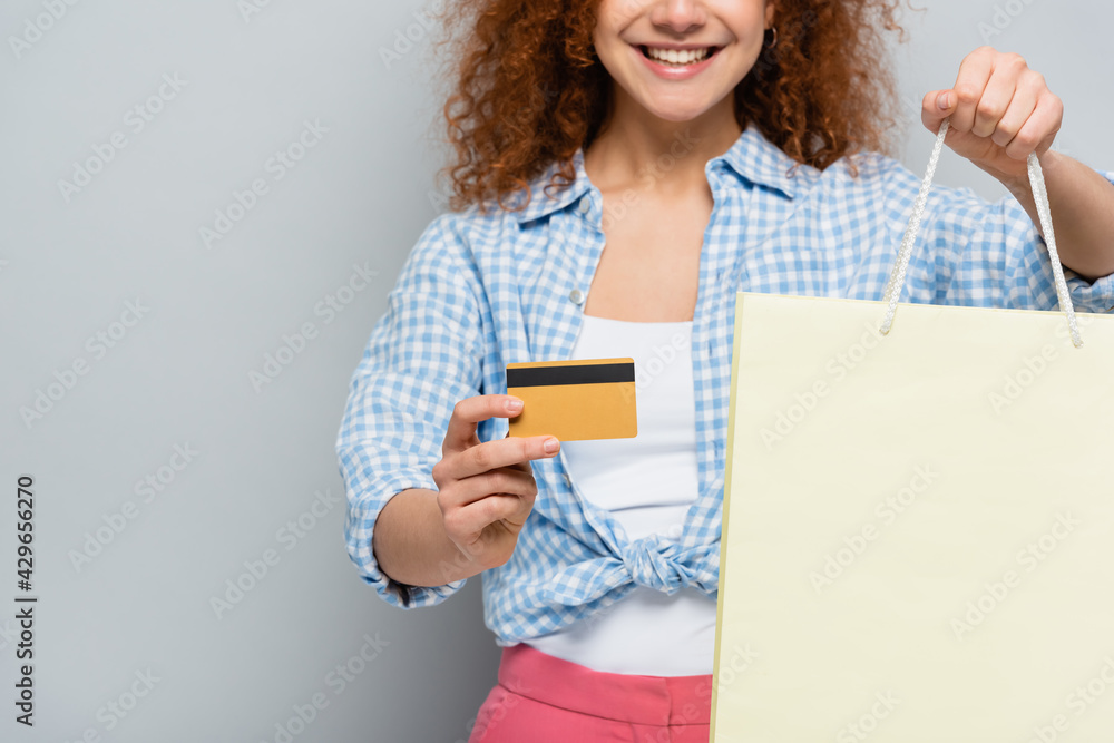 partial view of smiling woman with credit card and shopping bag on grey background partial view of smiling woman with credit card and shopping bag on grey background