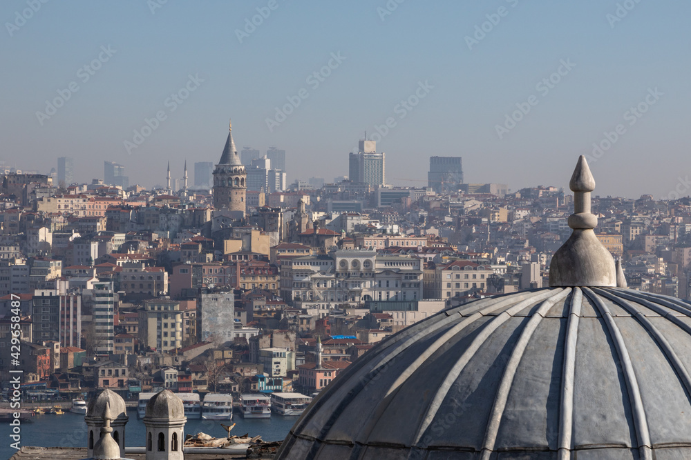 Panoramic urban cityscape of Istanbul from the rooftop of Suleymaniye Mosque. There are visible domes and chimneys of the mosque; Galata tower, Karakoy district, Golden Horn strait and sea transport.
