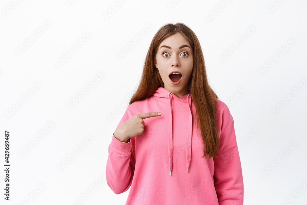 Image of excited and surprised woman points at herself, gasping and looking with disbelief, being chosen, winning something, standing over white background Image of excited and surprised woman points at herself, gasping and looking with disbelief, being chosen, winning something, standing over white background