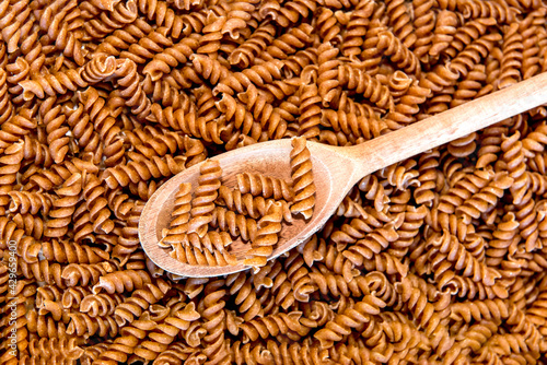 Wooden spoon with Raw wholemeal pasta, fusilli on Raw wholemeal pasta background with copyspace. Top view 