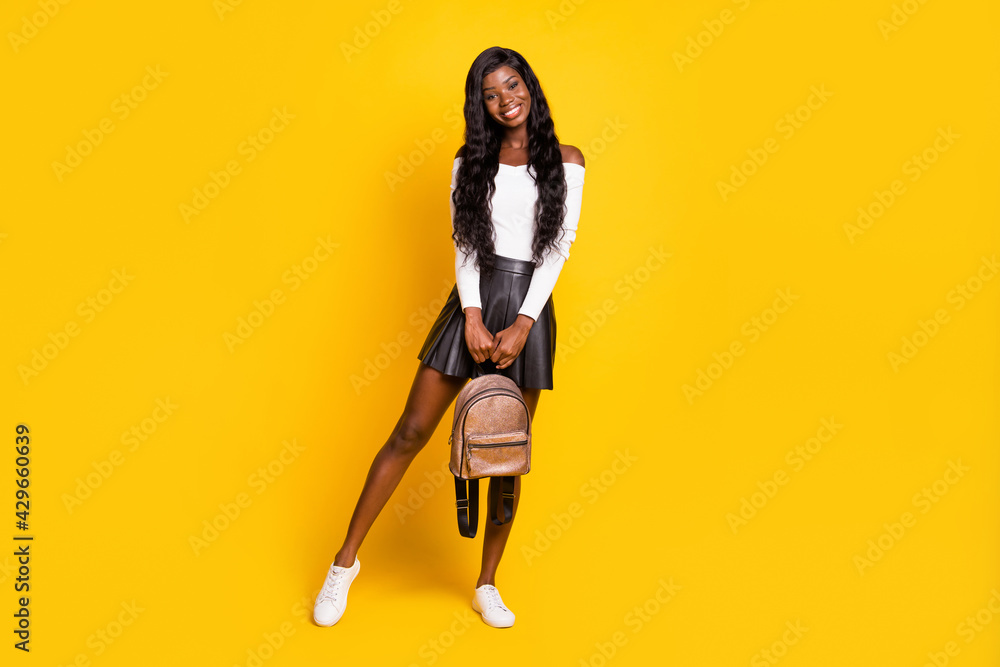 Full length body size photo black skinned brunette smiling holding rucksack wearing short skirt isolated on vibrant yellow color background Full length body size photo black skinned brunette smiling holding rucksack wearing short skirt isolated on vibrant yellow color background