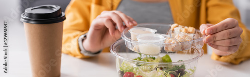 cropped view of teleworker near lunch box with salad and coffee on blurred background, banner