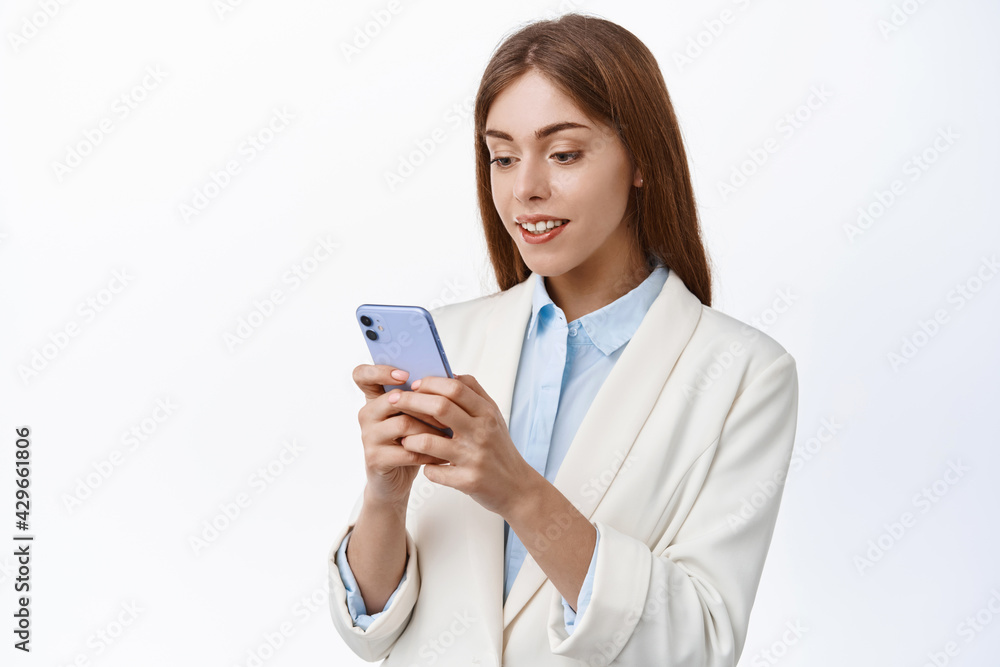 Professional ceo office woman reading mobile phone screen, standing in business suit and using smartphone app, standing with cellphone over white background Professional ceo office woman reading mobile phone screen, standing in business suit and using smartphone app, standing with cellphone over white background