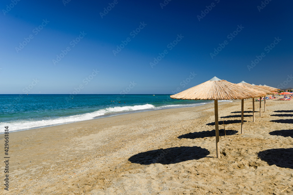 Fototapeta premium Turquoise sea white foam yellow sand deep blue sky footprints in sand, umbrellas