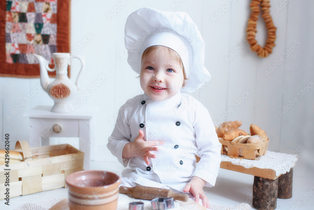 a little girl, blonde, in a white chef's hat, smeared in flour, with bagels around his neck, kneads dough in a brown wooden kitchen, prepares bread and pasta and tries everything a little girl, blonde, in a white chef's hat, smeared in flour, with bagels around his neck, kneads dough in a brown wooden kitchen, prepares bread and pasta and tries everything