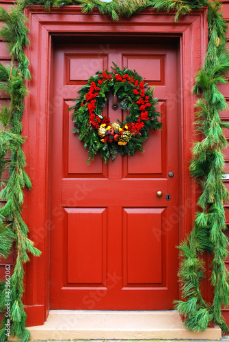 A Colonial door is decorated with traditional Christmas decor