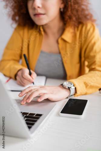 selective focus of smartphone with blank screen near freelancer working on blurred background