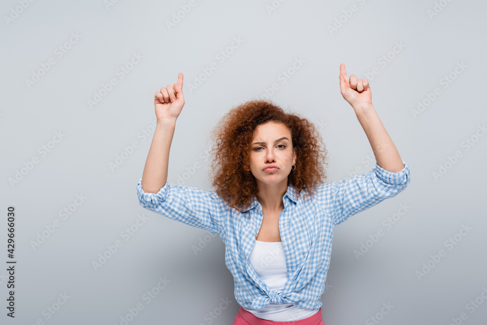 serious woman pointing up with fingers while looking at camera on grey background serious woman pointing up with fingers while looking at camera on grey background