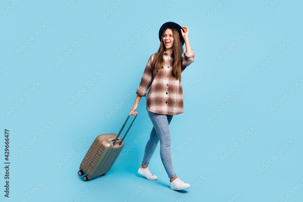 Full size profile side photo of young happy excited smiling girl go walk with luggage isolated on blue color background Full size profile side photo of young happy excited smiling girl go walk with luggage isolated on blue color background