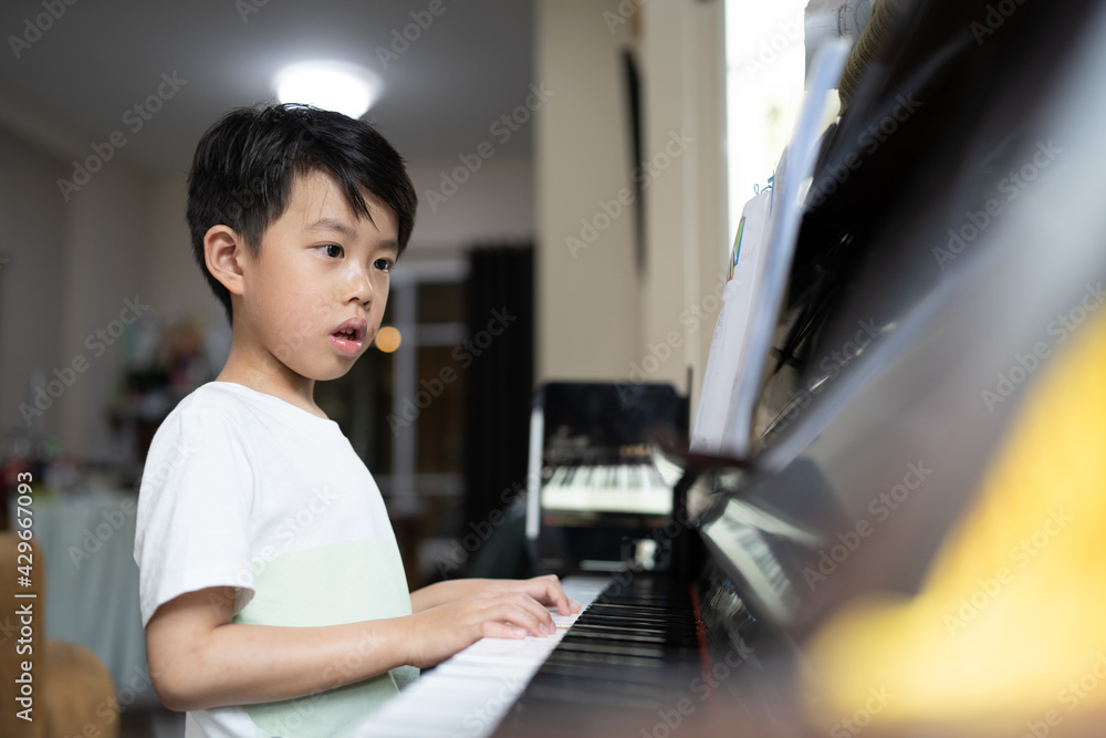 Fototapeta A boy is studying piano online with tablet.