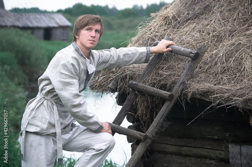 Downshifting concept. A young guy in national clothes lives in an eco-village and earns money from it