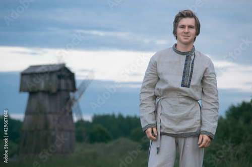 Downshifting concept. A young guy in national clothes lives in an eco-village and earns money from it