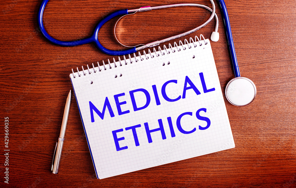 On a wooden table are a pen, a stethoscope, and a notebook labeled MEDICAL ETHICS. Medical concept On a wooden table are a pen, a stethoscope, and a notebook labeled MEDICAL ETHICS. Medical concept