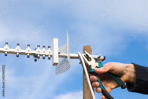 Installing directional antenna. Hands install TV antenna on blue sky background.