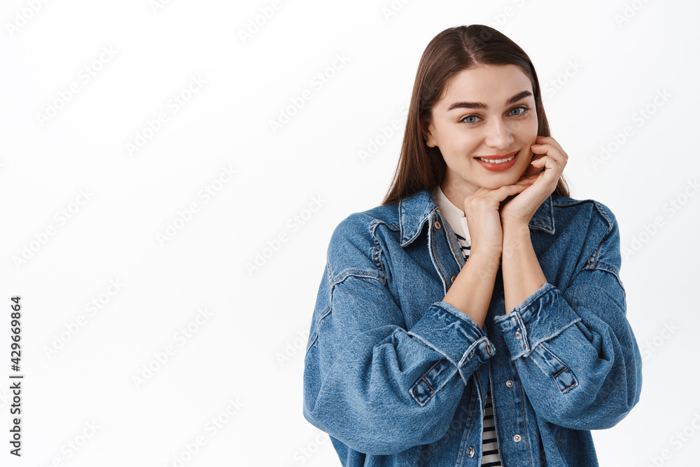 Tender smiling woman gently touching her face, holds hands near skin and smiles flirty at camera, making innocent angelic expression, standing over white background Tender smiling woman gently touching her face, holds hands near skin and smiles flirty at camera, making innocent angelic expression, standing over white background