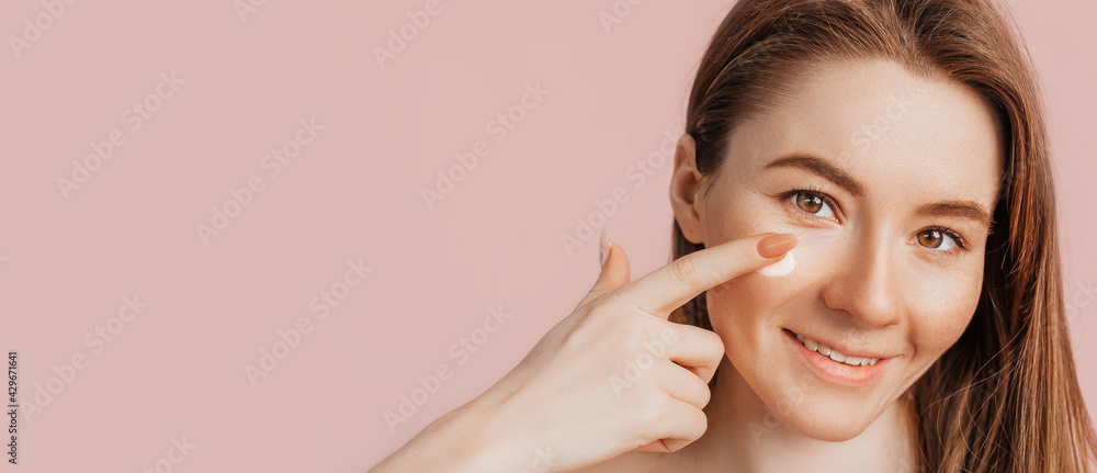 Girl make face beauty masks. Anti-wrinkle cream for the freshness of the skin around the eyes. Woman take care of youthful skin. Model laughing and having fun in spa on pink background Girl make face beauty masks. Anti-wrinkle cream for the freshness of the skin around the eyes. Woman take care of youthful skin. Model laughing and having fun in spa on pink background