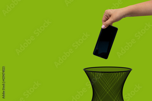 A hand holds a mobile phone over a trash can. The concept of technology obsolescence and recycling problems.