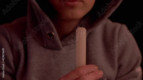 Woman Blows Out a Candle in Hands in a Dark Room. Supplication. White paraffinic candle with yellow fire. Flame, fire, smoke, extinction of fire. Concept of memory, ritual, celebration. Zoom. photo