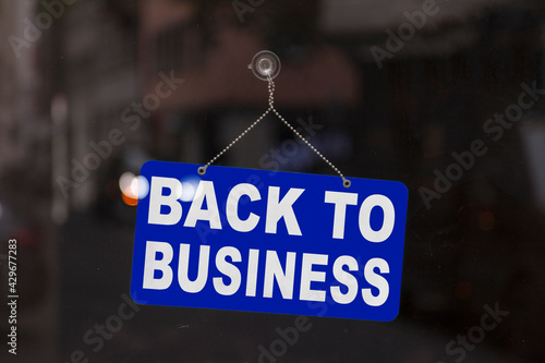 Close-up on a blue sign in the window of a shop displaying the message "Back to business".