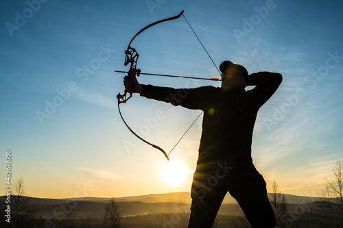 Silhouette of a hunter with a bow on a background of sunset. Hunting with arrows and a bow