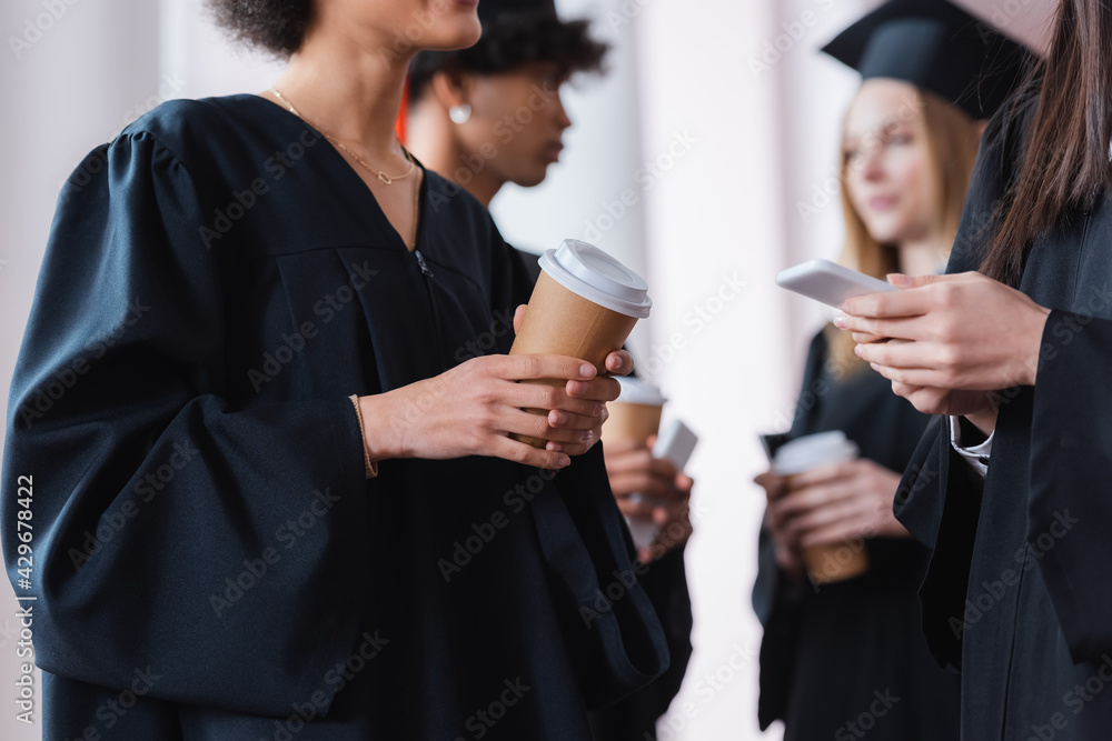 Multiethnic graduates holding coffee to go and smartphone Multiethnic graduates holding coffee to go and smartphone