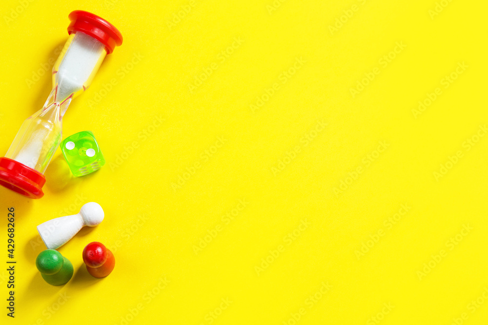 Layout of board games on a yellow background: dice, chips, hourglass timer. Entertainment at home for children and adults. Copy space Layout of board games on a yellow background: dice, chips, hourglass timer. Entertainment at home for children and adults. Copy space