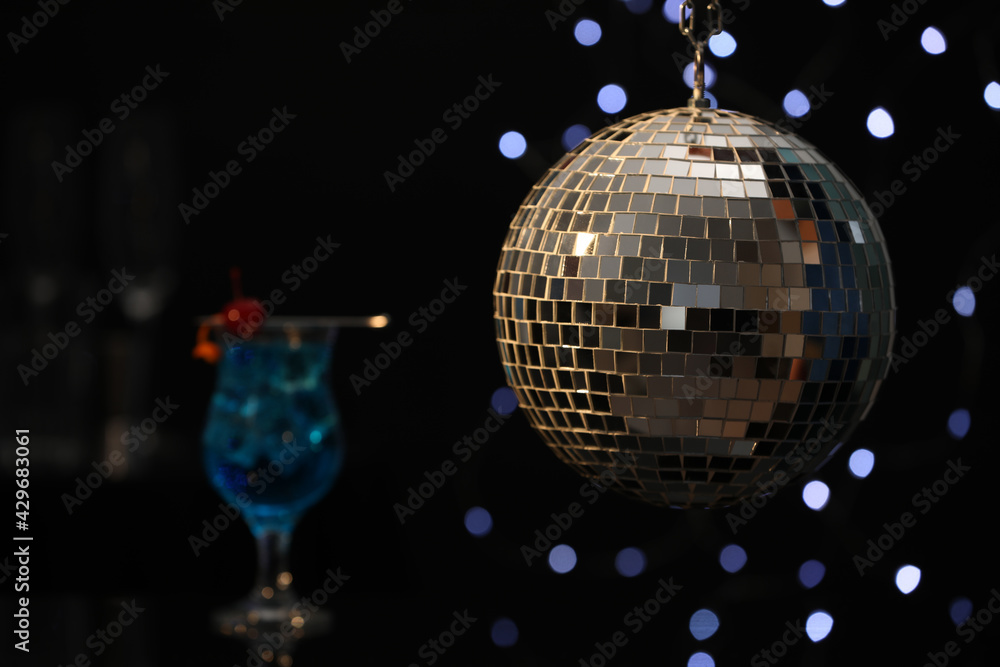 Obraz premium Shiny disco ball hanging over bar counter with cocktail in nightclub, space for text