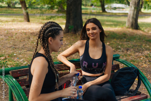 Two girls sit in a park while taking a break from rollerskating drinking smoothie,water and gossiping. Girls bonding concept. © qunica.com