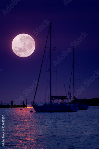 This beautiful pink Super Moonrise above the horizon over sailboats and harbor is a perfect night time illustration of this event.