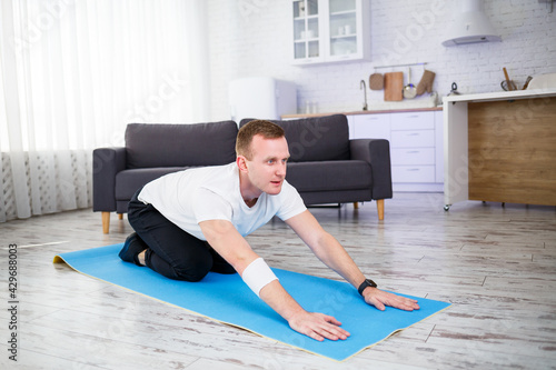 Young man sitting on carpet in his home and doing stretching after sports