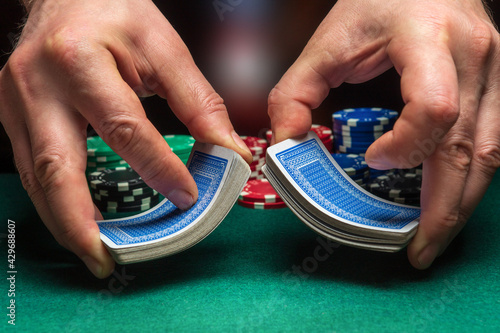Close-up hands of a person-dealer or croupier shuffling poker cards in a poker club on background of a table, chips. Poker game or gaming business concept
