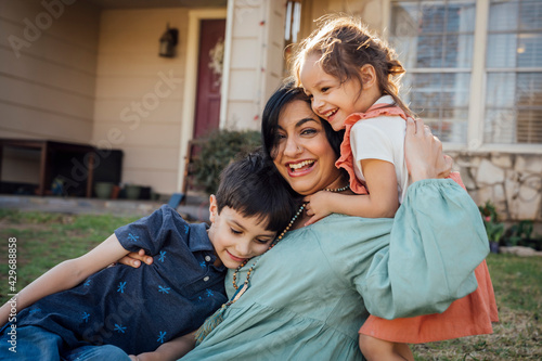 Mom sitting in front yard hugging kids in front of home