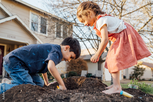 Girl and boy digging in dirt in front of home