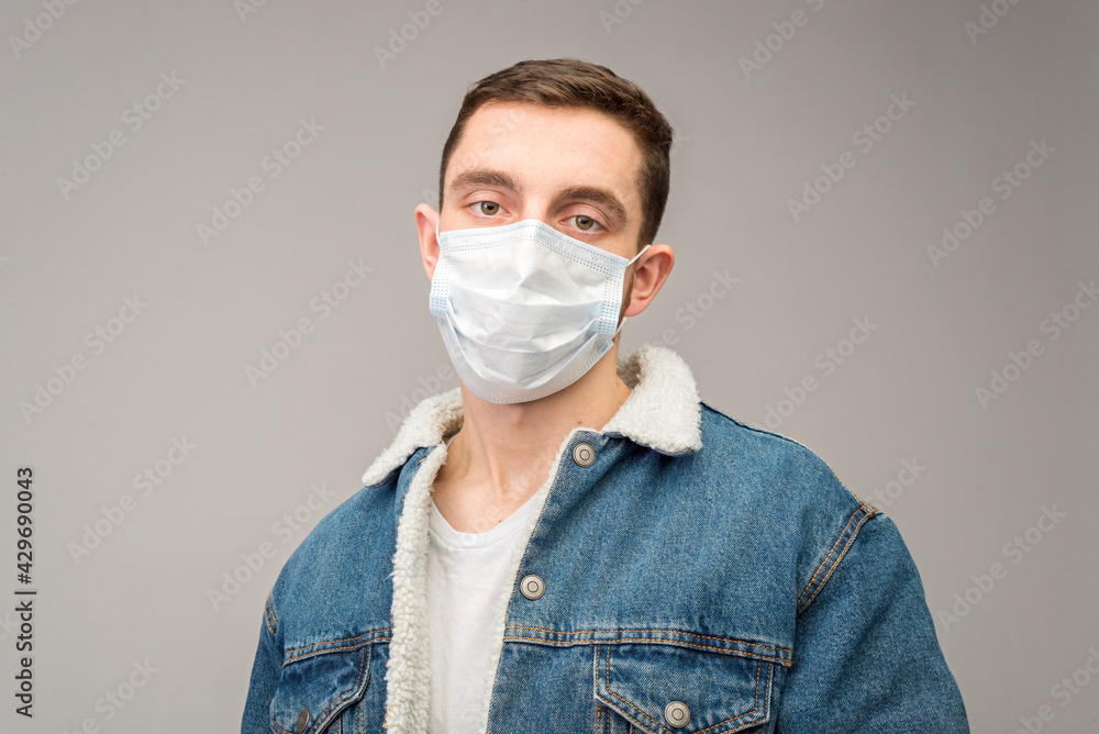 A young man on a light background in a medical mask protecting against the spread of coronavirus disease. Close-up of a man with a surgical mask on his face. A young man on a light background in a medical mask protecting against the spread of coronavirus disease. Close-up of a man with a surgical mask on his face.