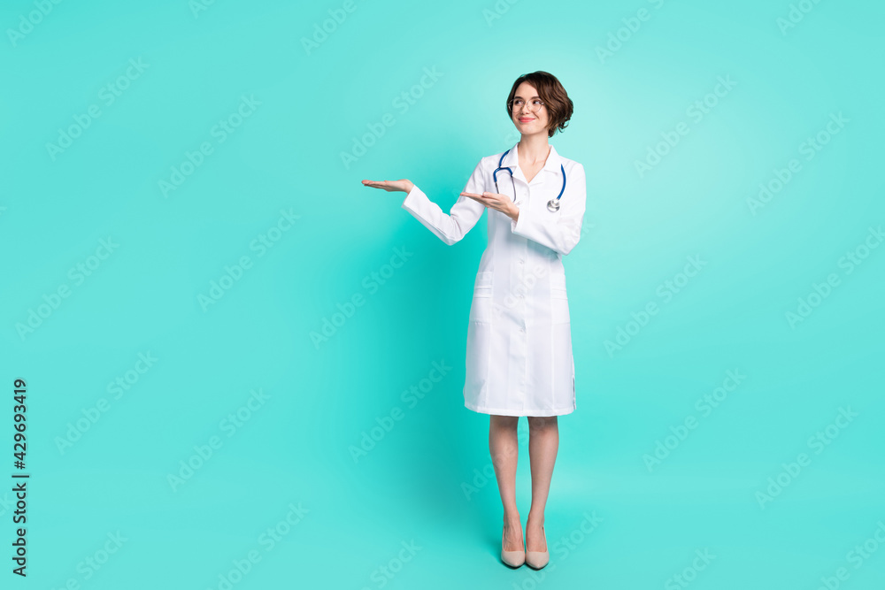 Full length body size photo of nurse smiling holding copyspace on hand in glasses isolated bright turquoise color background Full length body size photo of nurse smiling holding copyspace on hand in glasses isolated bright turquoise color background