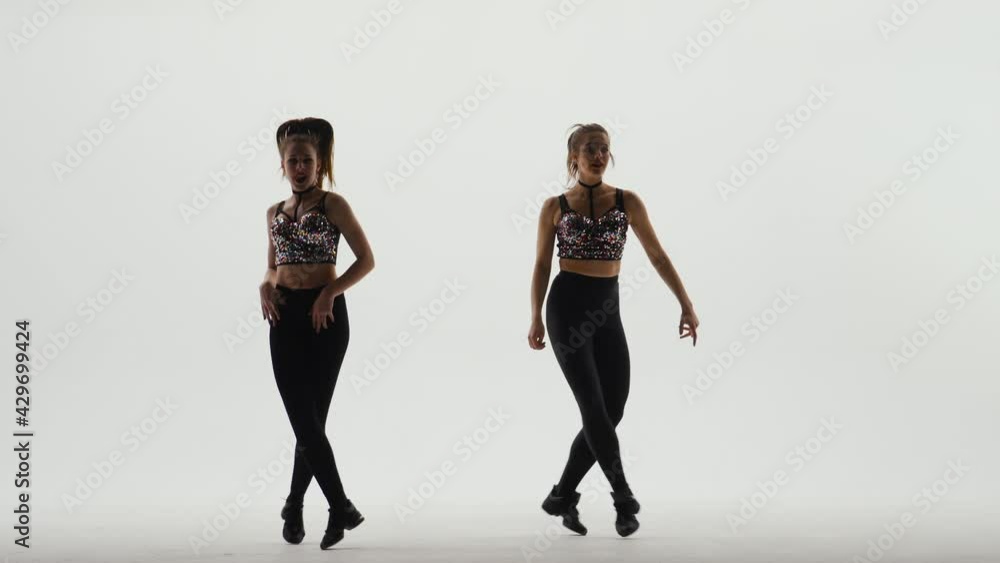 Two athletic cheerleaders in shiny tops and leggings are dancing in ...