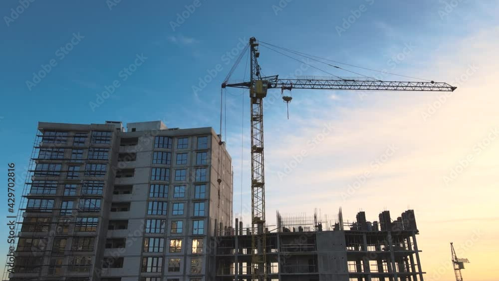 Aerial view of high tower crane and residential apartment building under construction at sunset. Real estate development. Aerial view of high tower crane and residential apartment building under construction at sunset. Real estate development.