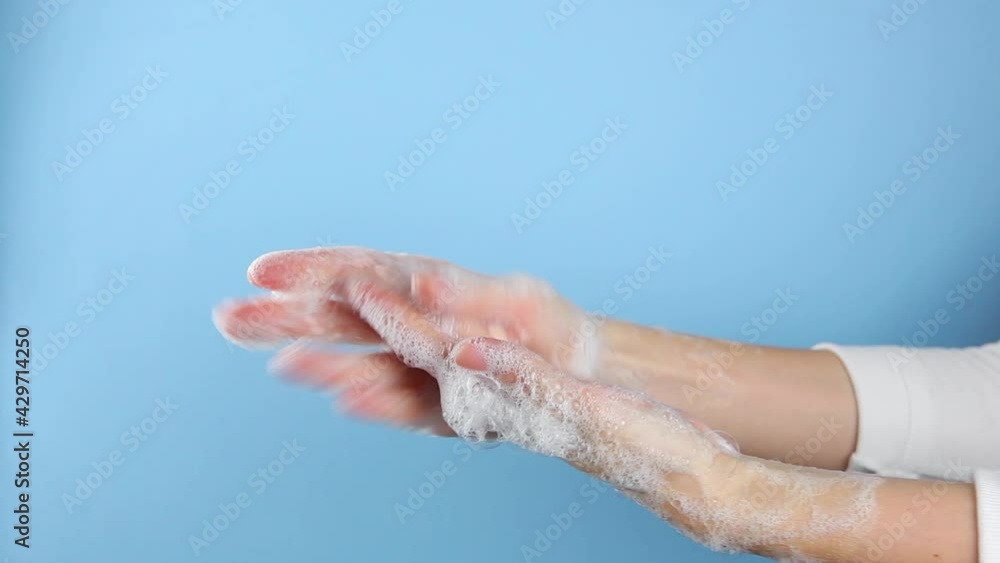 A woman lathers and washes her hands on a blue background close-up. A woman lathers and washes her hands on a blue background close-up.