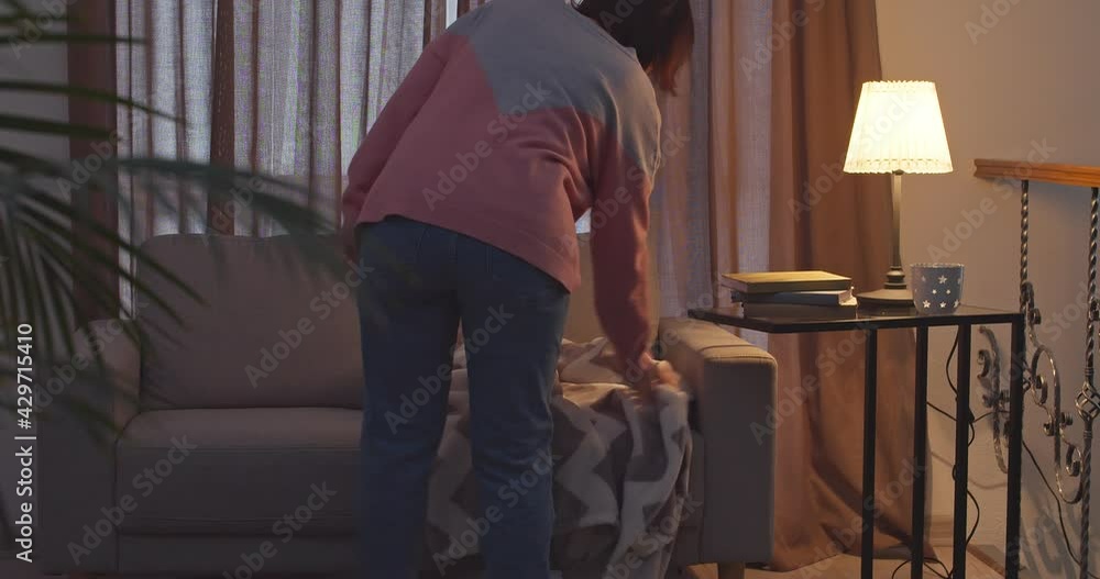 Young woman putting soft plaid on sofa Young woman putting soft plaid on sofa