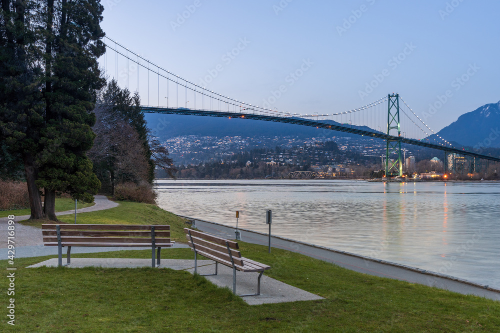 Stanley Park Seawall wooden bench. Lions Gate Bridge In the background at twilight. Vancouver, British Columbia, Canada.