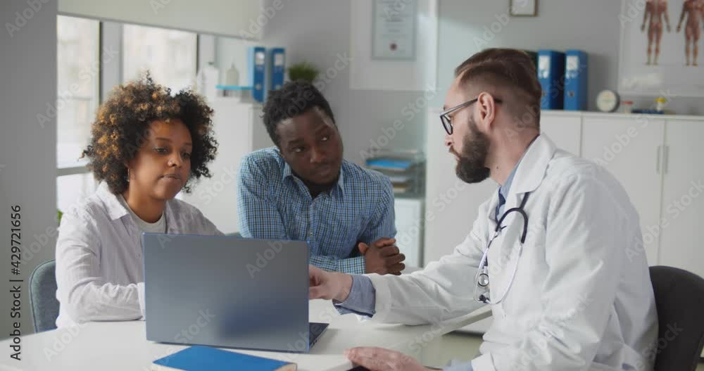 African couple looking at ultrasound baby image on screen of laptop at doctor office