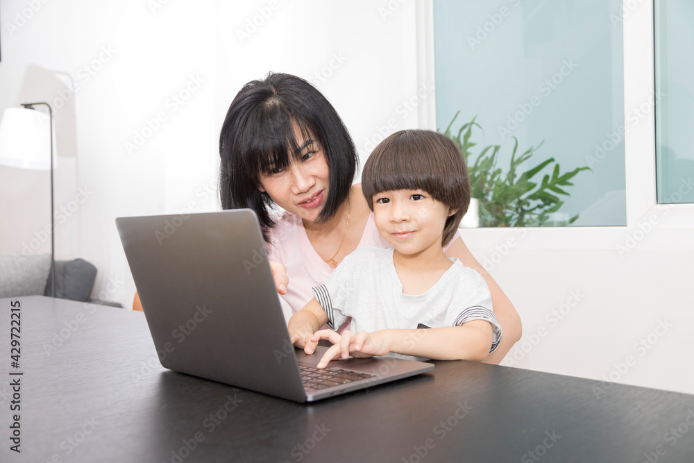Asian woman with a child works on computer. Concept of work from home and home family education. Mom and son are working on a laptop at home. Asian woman with a child works on computer. Concept of work from home and home family education. Mom and son are working on a laptop at home.