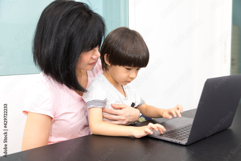 Asian woman with a child works on computer. Concept of work from home and home family education. Mom and son are working on a laptop at home. Asian woman with a child works on computer. Concept of work from home and home family education. Mom and son are working on a laptop at home.