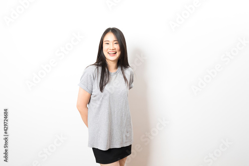 Portrait of happy young asian woman wearing grey shirt smiling at camera while standing over white background. © bennnn