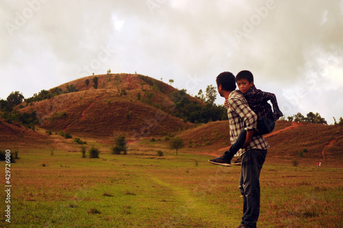 Father carrying his son are walking on the field at the Phu Khao Ya (Grass hill) in Ranong province of Thailand on evening day. 
