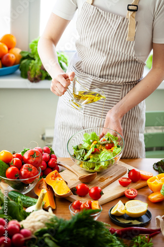 Beautiful young woman preparing delicious fresh vitamin salad with olive oil. Concept of clean eating, healthy food, low calories meal, dieting, self caring lifestyle. Colorful vegetables. Close up