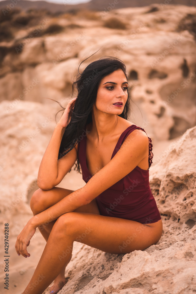 Portrait of a young brunette Caucasian woman in a maroon swimsuit, sitting smiling on the beach of Cabo de Gata, Nijar. Andalucia, Spain Portrait of a young brunette Caucasian woman in a maroon swimsuit, sitting smiling on the beach of Cabo de Gata, Nijar. Andalucia, Spain