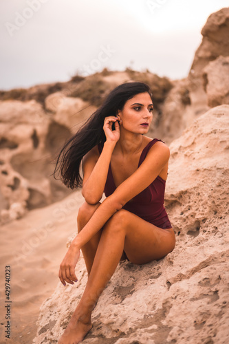 A young brunette Caucasian woman in a maroon swimsuit, sitting on the beach of Cabo de Gata, Nijar. Andalucia, Spain