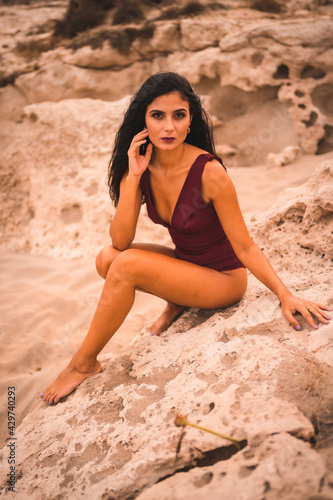 Sweet look of a young brunette Caucasian woman in a maroon swimsuit, sitting smiling on the beach of Cabo de Gata, Nijar. Andalucia, Spain photo